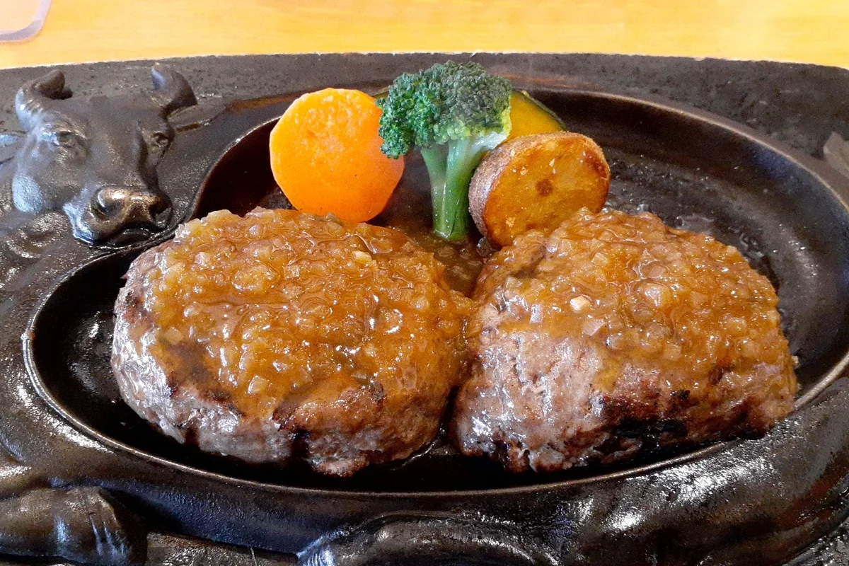 鉄板に並んだ2つのハンバーグと、ブロッコリー・にんじん・じゃがいもを添えた、さわやかのげんこつハンバーグ