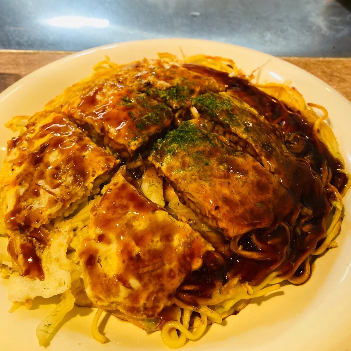 みっちゃん総本店で提供された、ソースと青のりをかけた麺入りのお好み焼き
